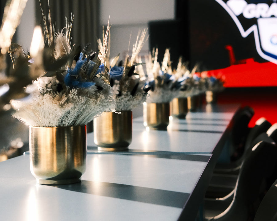 Dried and preserved bouquets of blue, white and cream flowers in gold vases along a long table.